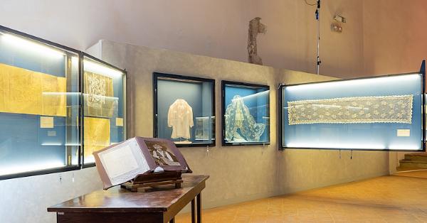  Display cases containing tulle artifacts and historical documents. In the foreground, an open book on a table with a photograph. 